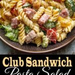 Bowl of creamy Club Sandwich Pasta Salad made with rotini pasta, diced ham, crispy bacon, cherry tomatoes, cucumbers, cheddar cheese, and lettuce, topped with seasoned croutons, served on a rustic plate.